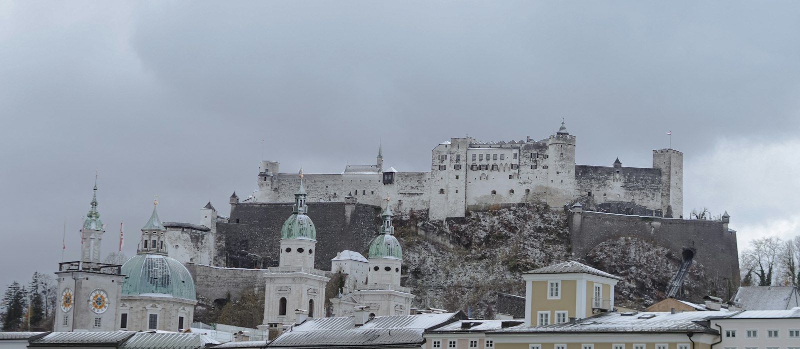 Hohensalzburg fortress above the snow-dusted roofs and green church domes of the Salzburg old town on an overcast winter day